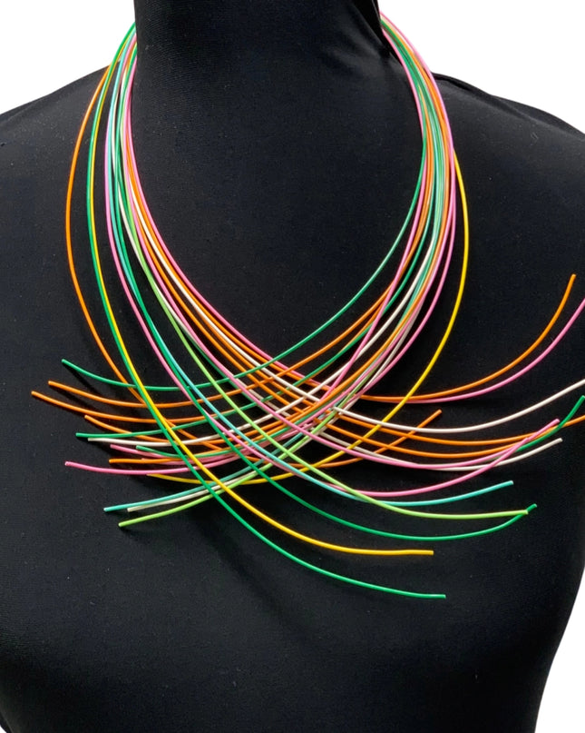 A multi-colored necklace displayed on a mannequin, featuring numerous slender wires in various colors arranged in a layered pattern.