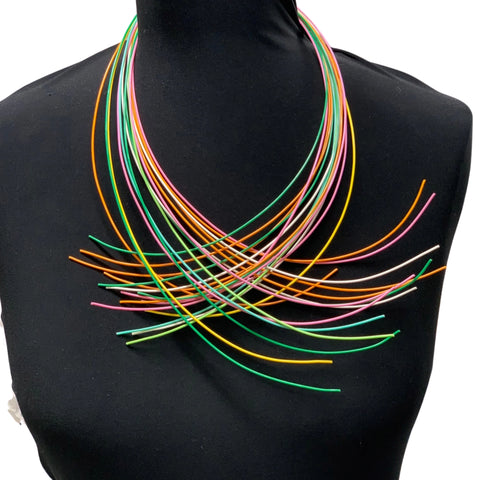 A multi-colored necklace displayed on a mannequin, featuring numerous slender wires in various colors arranged in a layered pattern.
