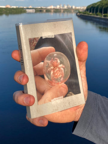 A hand holding a book titled 'oberih' with a reflective surface and an image of a protective item encased in a clear dome on the cover.