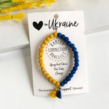 A bracelet with blue and yellow beads, and a tassel, displayed on a card with text supporting Ukraine.