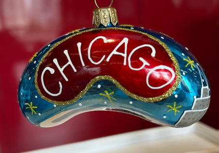 A hand-painted glass Chicago-themed ornament shaped like a curved game piece, featuring a red center with white 'CHICAGO' lettering, a blue outer section with gold stars, and a silver-and-blue cityscape detail, hanging against a red and beige background.