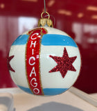 A spherical Christmas ornament featuring the Chicago flag design, with a vertical red banner reading 'CHICAGO' and two red glitter stars, hanging against a red background.