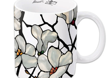 A white ceramic coffee mug with a floral design featuring magnolias, with a printed signature of Louis C. Tiffany.