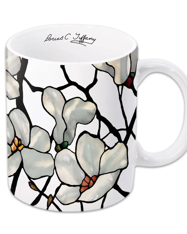 A white ceramic coffee mug with a floral design featuring magnolias, with a printed signature of Louis C. Tiffany.