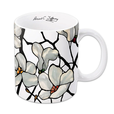 A white ceramic coffee mug with a floral design featuring magnolias, with a printed signature of Louis C. Tiffany.